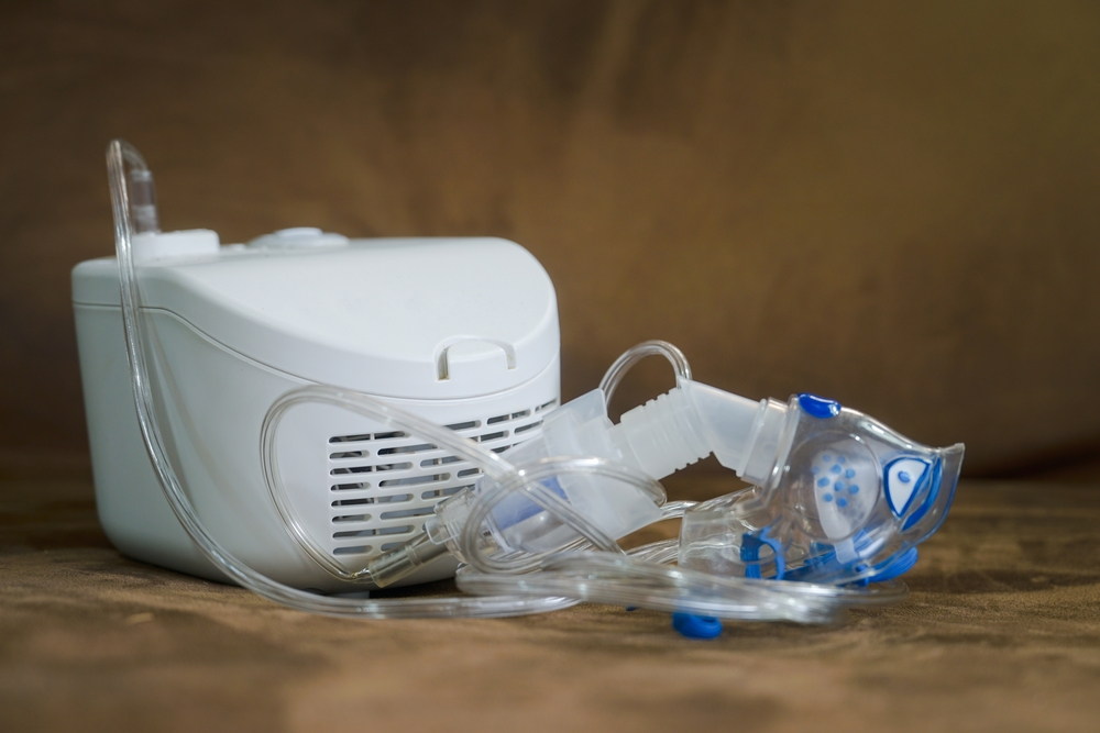 A white compressor nebulizer machine with clear plastic tubing and a blue-accented respiratory face mask.